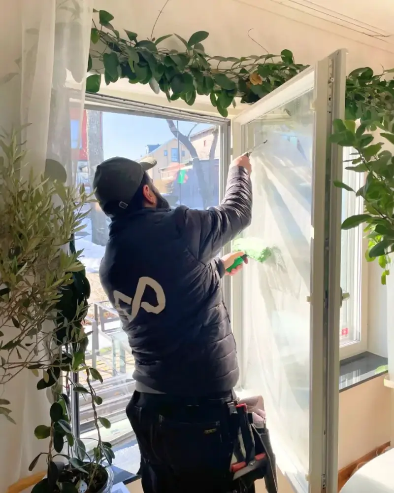 bvtler-medarbetare som putsar ett fönster inifrån i starkt vinterljus.